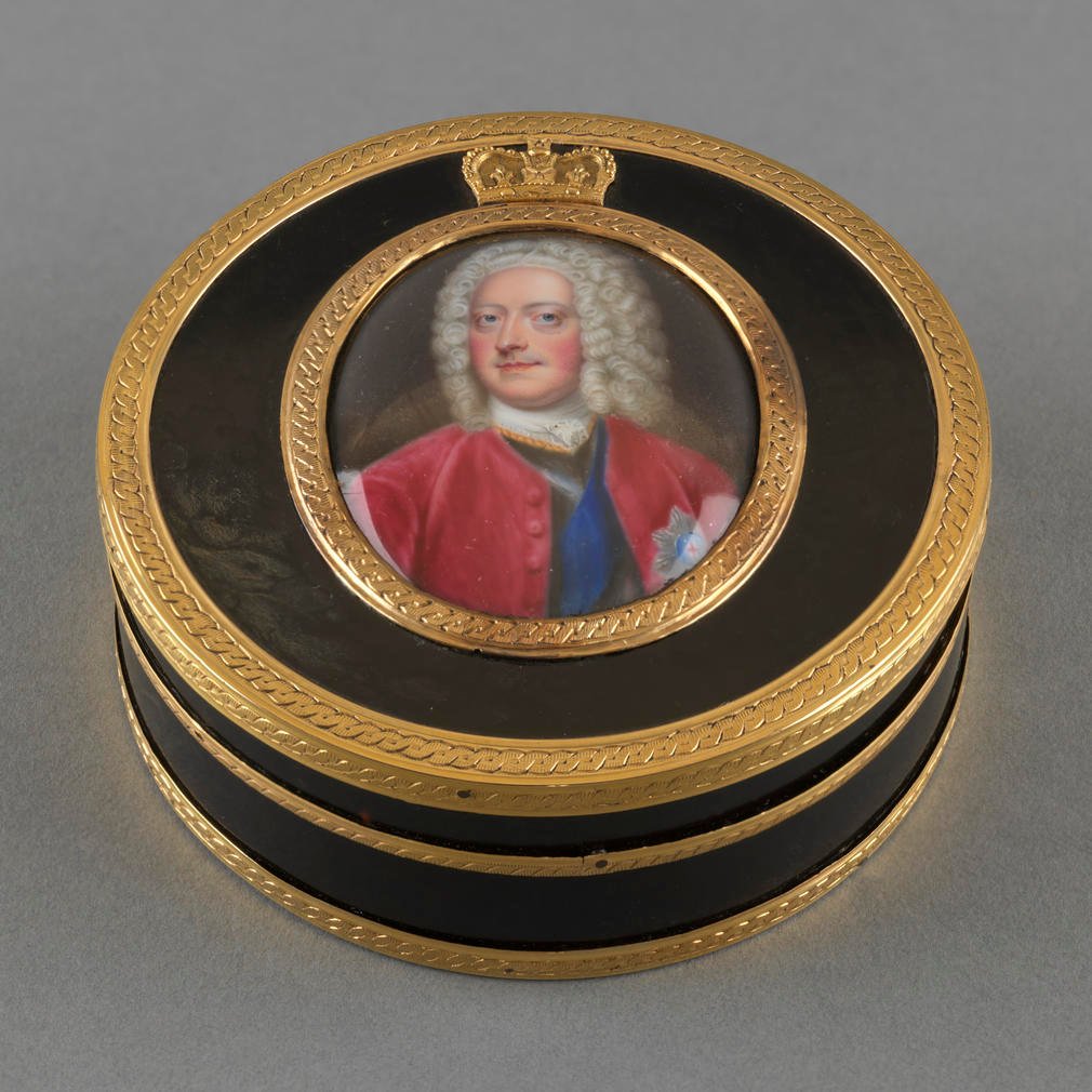 Circular tortoiseshell box and cover, with gold mounts, with inset glazed enamel miniature of George II: bust-length; facing slightly right, his head turned half left and looking forwards; wearing a crimson coat over armour and the ribbon and star of the 