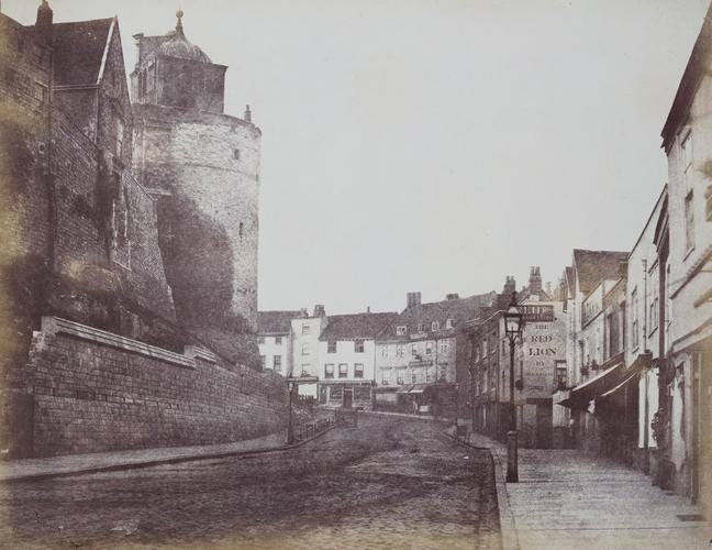 View of the Castle wall along Thames Street in Windsor, Curfew Tower to left of street. [Windsor Castle]