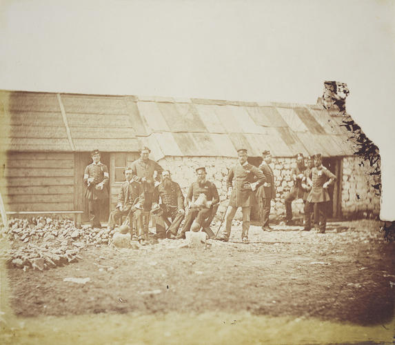 Group outside a hut, with two cannonballs on blocks