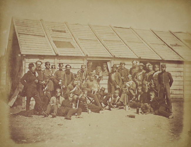 Group outside row of huts with two dogs, bottles and tankards. [taken from contents list]. [Crimean War photographs by Robertson]